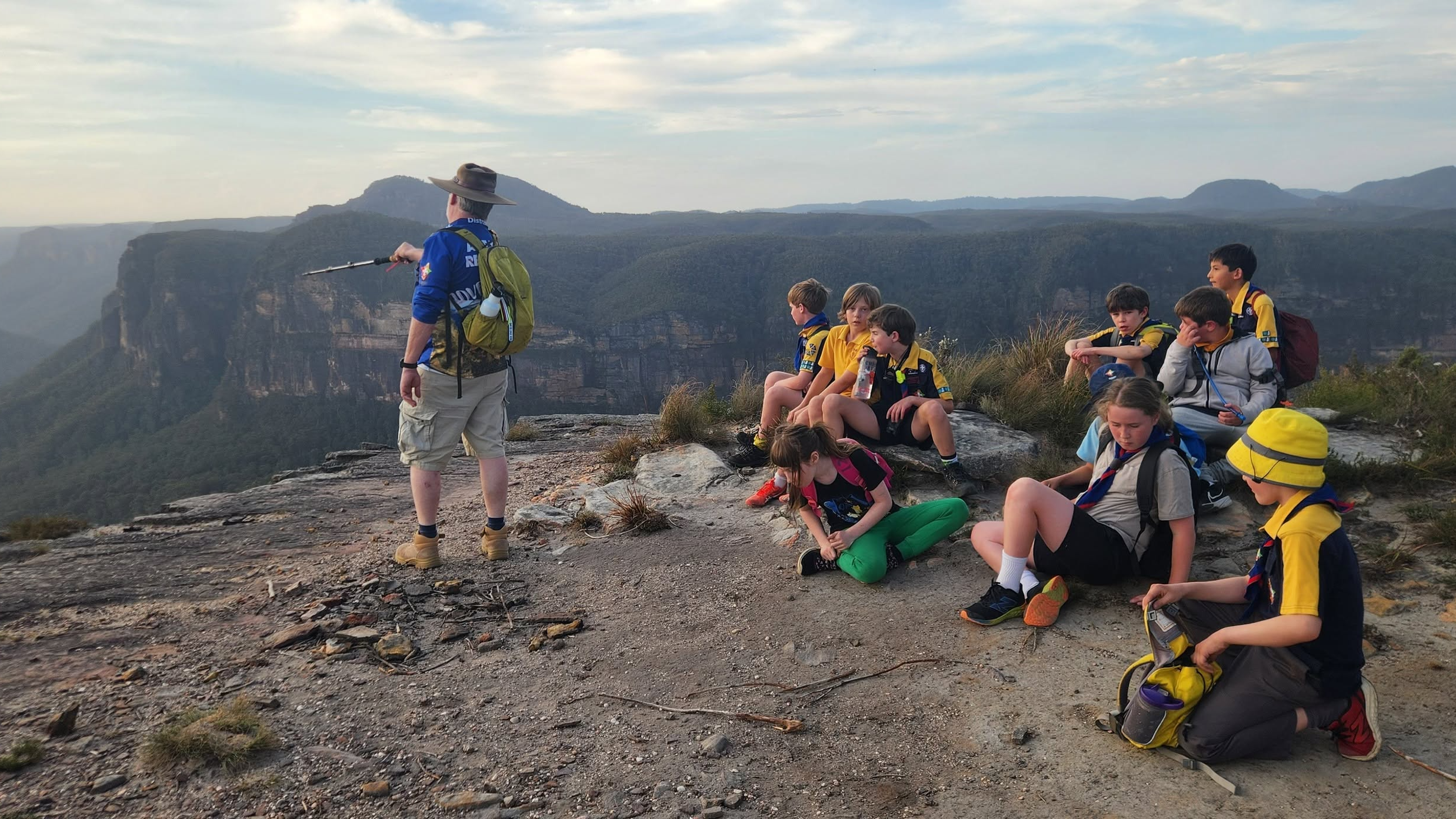 A Leader pointing out the view across the escarpment to a group of Scouts resting at a clifftop lookout